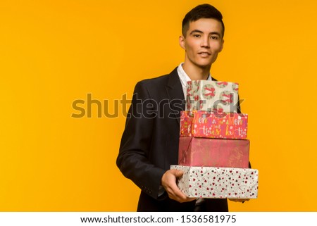 Handsome asian businessman holding gift box over yellow background - image