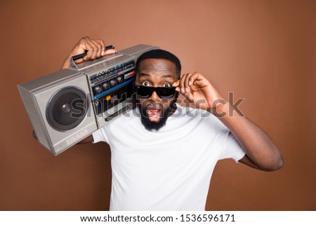 Photo of astonished casual man holding retro audio recorder wearing white t-shirt and eyewear sunglass isolated over pastel color brown background listening to music