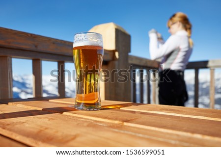 Glass of beer in the snowy mountains, woman taking pictures of the scenic landscape view