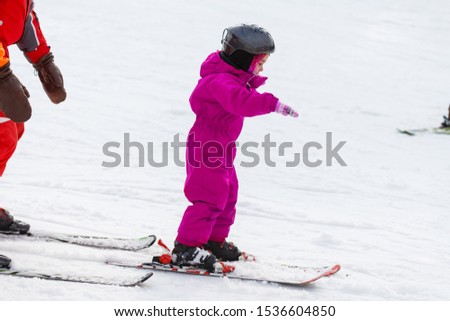 little girl learns to ski with the help of an adult