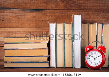Red clock alarm clock, old books and textbooks on the bookshelf, educational concept.