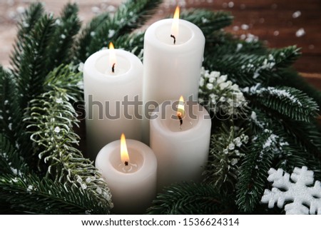Christmas candles with fir tree branches and snowflakes on brown wooden table