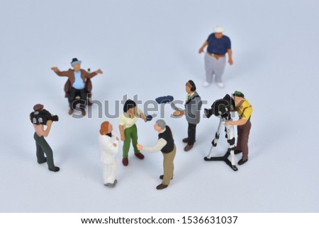 miniature people are discussing in front of a camera crew