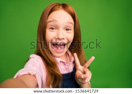 Closeup photo of pretty little foxy lady showing v-sign symbol making selfies excited cheerful mood wear denim overall pink shirt isolated green background