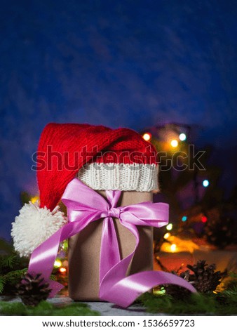 Christmas and new year gift box Packed in Kraft paper in Santa hat on blue background with Christmas tree branches and garland