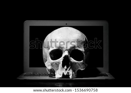 Cybercrime or hacking concept. Laptop in dark room under beam of light with a skull. Idea of virus or worm program cyber attack. Royalty-Free Stock Photo #1536690758