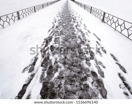 Footprints in the fresh snow on the asphalt track in winter. Icy sidewalk with snow, a footpath with a small fence along them.