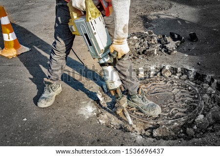 A man works with an electric jackhammer, smashes asphalt.