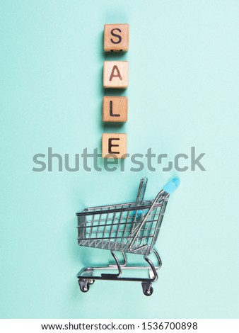 A miniature shopping cart and wooden blocks with the wordings SALE, isolated against mint background.