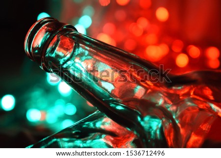 A picture showing an empty bottle resting on another empty bottle, in front of a bokeh background.