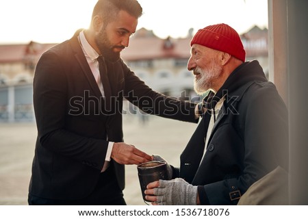 Man in tuxedo came up to beggar to help, give money donation. Rich man hold out his hand with money to homeless person. People relationship concepr Royalty-Free Stock Photo #1536718076