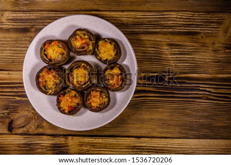 Baked champignons stuffed with minced meat and cheese in plate on wooden table. Top view