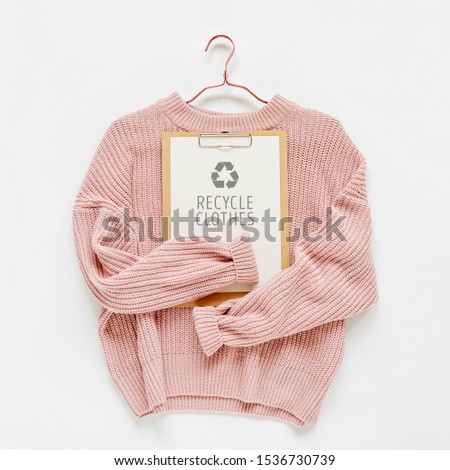 Recycle clothes concept. Pale pink knitted sweater with clipboard  on white background. Autumn and winter clothes. 