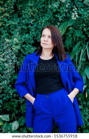 A young cute girl in a blue suit posing in front of background of green leaves. Portrait of a young woman