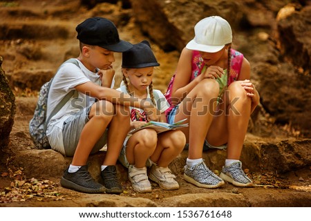 Kids navigating on map during treasure hunt games. Little boy and two girl go hiking on a forest road