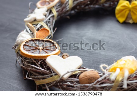 Christmas wreath made of birch branches, dried citrus, clay figurines (heart, bear), nuts, acorn and yellow bow, tied up with gold ribbon. Close-up.