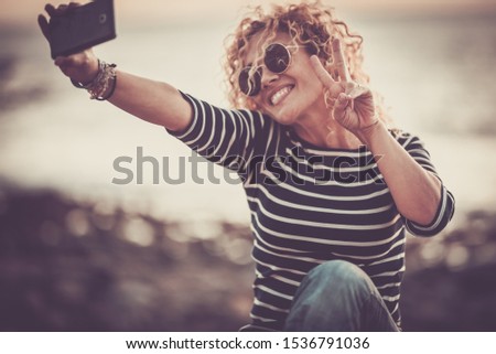 Cheerful happy beautiful curly trendy woman taking selfie picture with modern phone - people enjoying the outdoor technology leisure activity -   defocused beautiful background