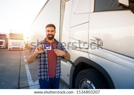 Truck driver standing by his truck and holding driving license. Professional drivers wanted. Transportation service. Royalty-Free Stock Photo #1536803207