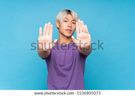 Young asian man over isolated blue background making stop gesture and disappointed