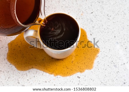 Coffee pours into mug overflows and spills over with too much spilling on white kitchen counter Royalty-Free Stock Photo #1536808802