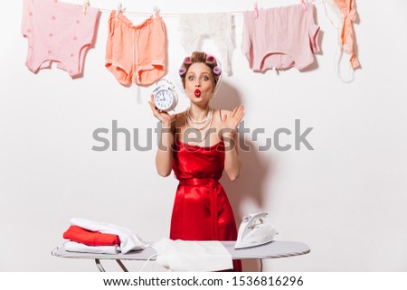 Beautiful woman in home clothes of red color and white pearls around her neck holding big alarm clock