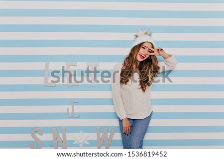 stylish, self-confident woman of 24 years old poses joyfully, showing sign of peace. Portrait on background of inscription with beautiful font