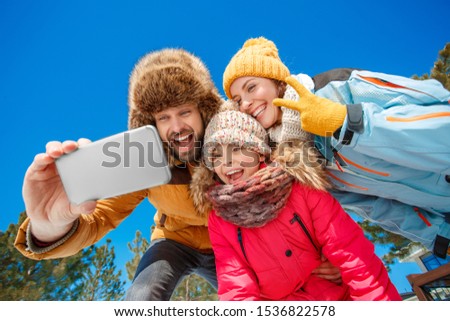 Family on a winter vacation spending time together outdoors taking selfie photo on smartphone grimacing to camera smiling playful bottom view
