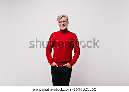 Smiling handsome male model in glasses posing with hands in pockets. Indoor shot of emotional old man isolated on white background.