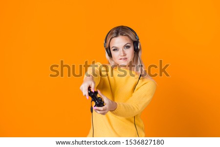 Girl gamer. Play computer games, a modern hobby and sport. A young woman with a gamepad on a yellow background