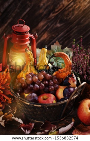 rustic autumn decoration with wicker basket full of seasonal fruits, gourds and leaves on wooden table
