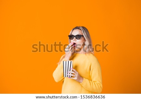 Young cheerful woman in 3D glasses watching a movie and eating popcorn. Fan of the movie, copy space