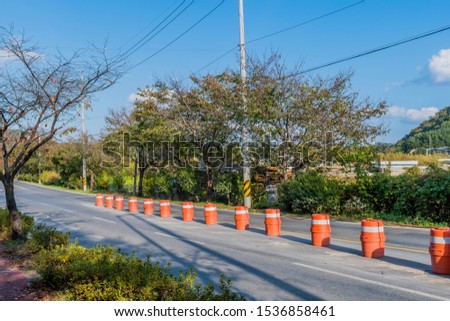 Orange traffic barrels next to double yellow line on paved road.