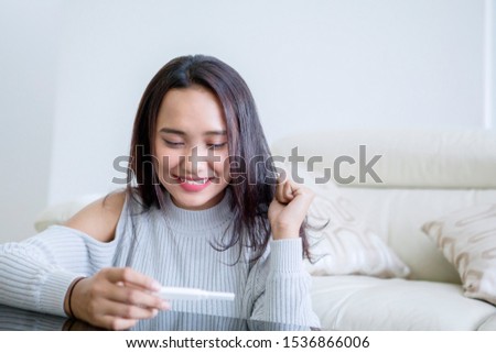 Picture of teenage girl looks happy while holding a pregnancy test while sitting in the living room