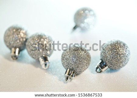 Silver Christmas-tree decorations on a white surface imitating freshly fallen snow and snowdrift. Happy New Year and Merry Christmas. Minimalism. Bokeh. Shallow depth of field.