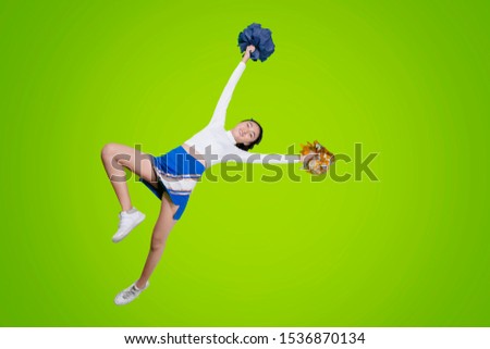 Low angle view of cheerleader girl dancing with pom poms while jumping in the studio