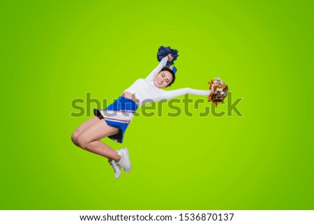 Low angle view of pretty cheerleader performing dances with pom poms while jumping in the studio