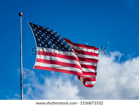 American flag waving in the wind against a blue sky with clouds