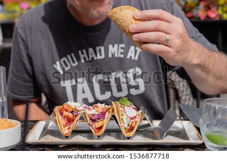 closeup of man eating gourmet shrimp tacos at outdoor restaurant in summer