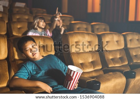 Asian boy go to the cinema. Alone in theater so bored movie and sleeping on a yellow sofa after eating popcorn. Background with couple people.