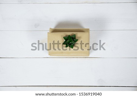 An overhead shot of a present with a green bow on a white wooden surface