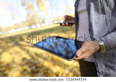 Man in pakr hold digital tablet pc in park against yellow leaves background closeup. Autumn sales concept