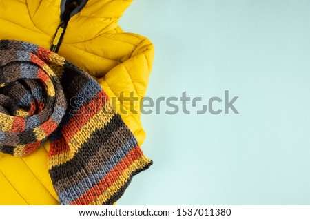 Yellow kids winter jacket composition on blue background. Flat lay, layout and tabletop mockup with copy space.