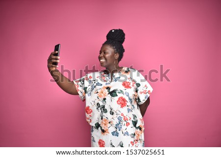 pretty plus-size african lady smiling and looking at her phone she is holding at a distance, taking a selfie