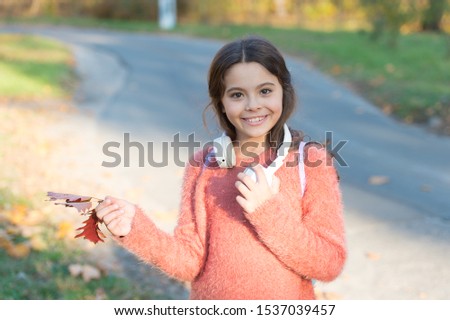 Music of autumn leaves. Happy little girl wear headphones on autumn landscape. Cute child smile with ear stereo headphones. Small kid with modern headphones. Headphones technology.