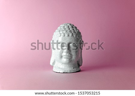 Ceramic head of a Buddha on a pink background. Minimal concept, copy space.