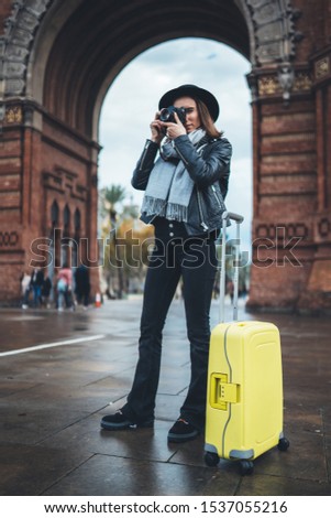 Photographer tourist with retro photo camera. Girl in hat travels in Triumphal arch Barcelona. Holiday concept in europe city street . Traveler hipster shooting architecture, copy space mockup