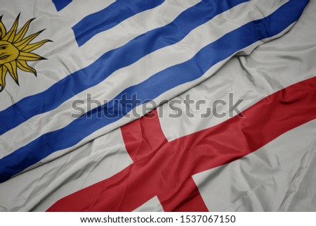 waving colorful flag of england and national flag of uruguay. macro