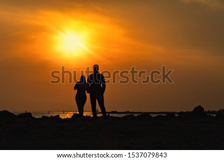two silhouettes of man and woman are standing next to rear view on elevation and looking at Gulf of Finland with sailboats sunset