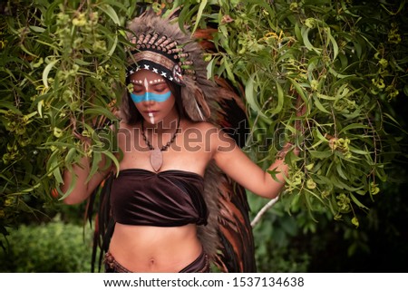 The beautiful woman wearing headdress feathers of birds. American Indian girl in native costume,posing in forest