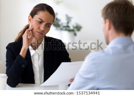 Doubtful mixed race female human resources manager looking through resume, unsure about male job applicant working experience, head shot. Frowning frustrated employer feeling confused on interview. Royalty-Free Stock Photo #1537134941